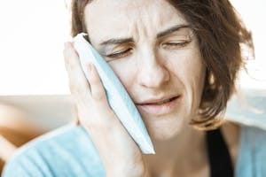 A woman who appears to be experiencing a toothache holds an ice pack to her cheek.