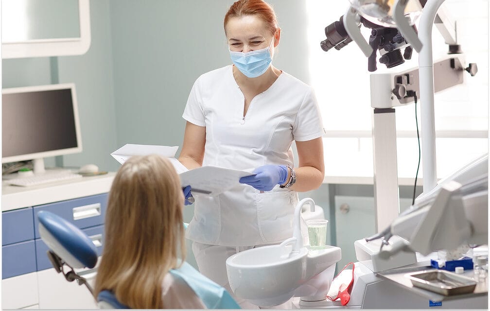Masked dentist reviewing paperwork with a patient.