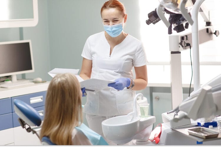 Masked dentist reviewing paperwork with a patient.